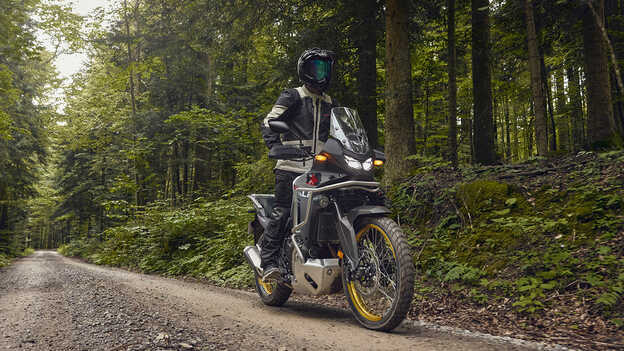 Model na motocyklu Honda XL750 Transalp v lesní lokalitě.